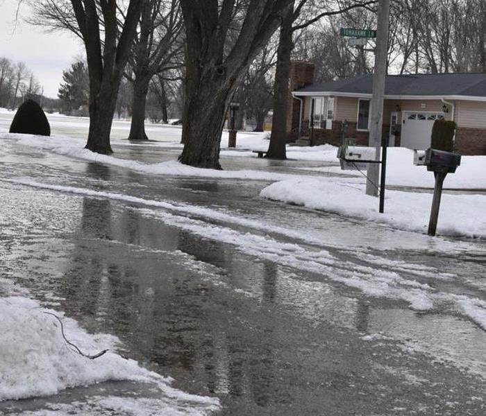 A local street with water caused by snow melting running down the streets and into residential areas.